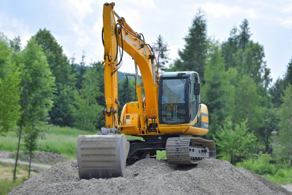 Ein gelber Bagger auf einem Kieshaufen in einer üppigen, grünen Waldlandschaft in Polen.