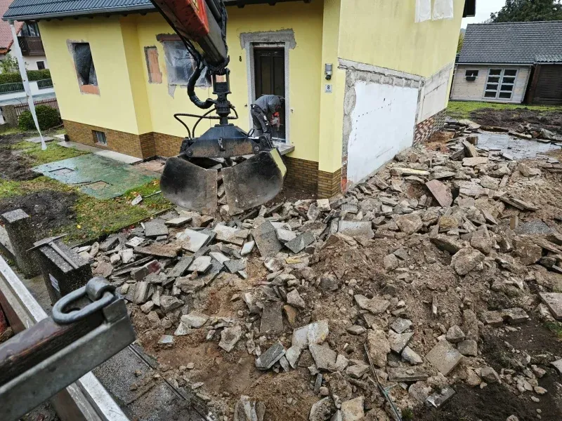 Bagger hebt Steine neben Haus